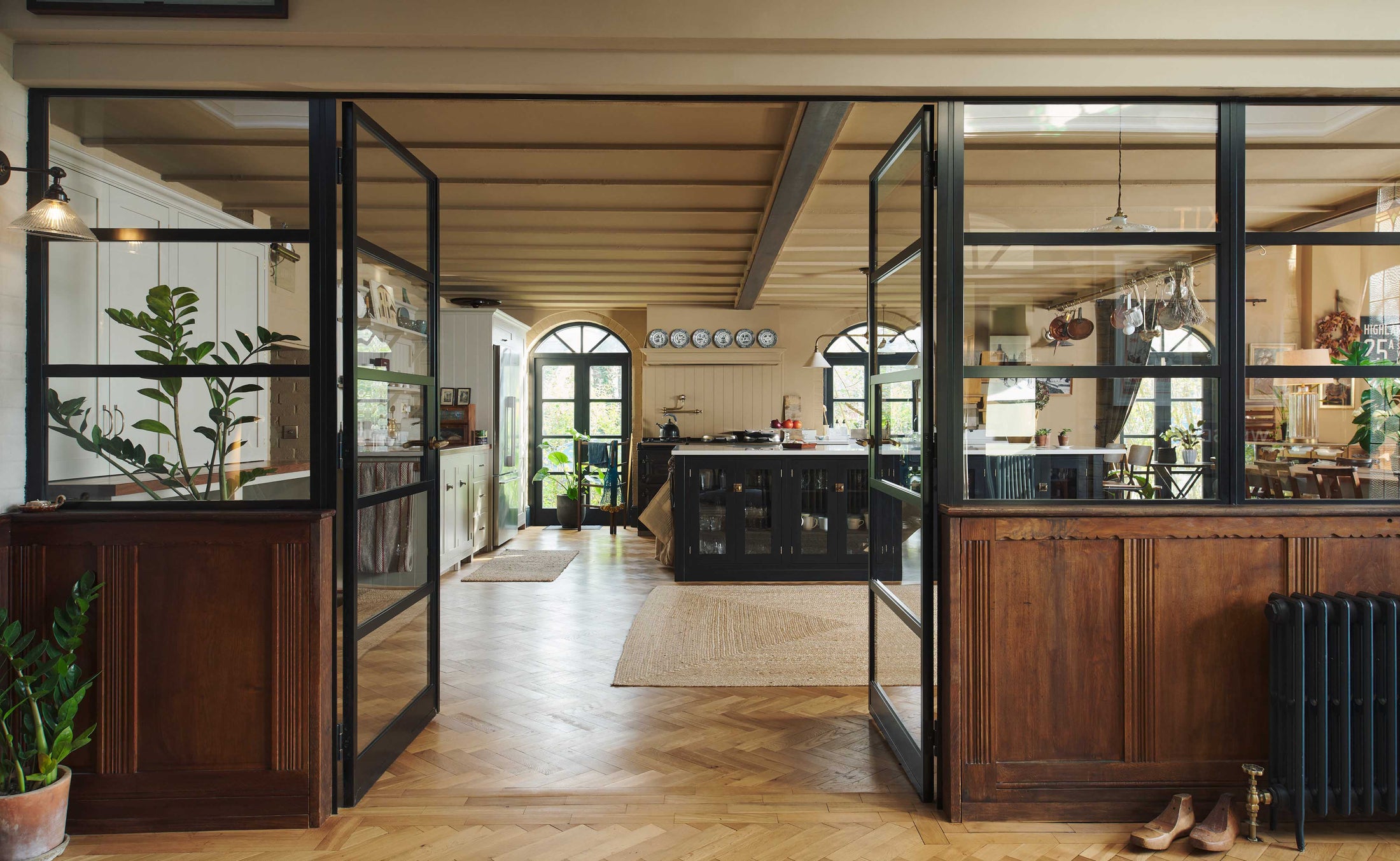 Past through the glass partitions, is a wide open social space that includes a Painter's black Shaker kitchen and Mushroom pantry. Busy with a lot of kitchen utilities, plants, and beloved furniture and ceramics, the space is an incredibly inviting and comfortable family room.